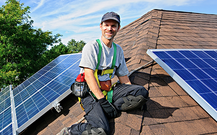 Solar technician smiling at camera while installing solar panels on roof of residential home
