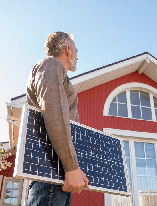 Man carrying solar panel next to the front of a red house