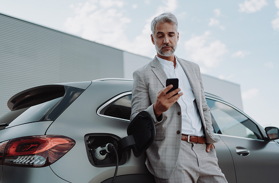 Business man wearing a suit checking his phone why charging his electric vehicle