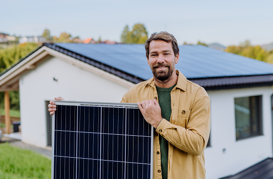 Happy man standing infron of a solar powered home while holding a solar panel